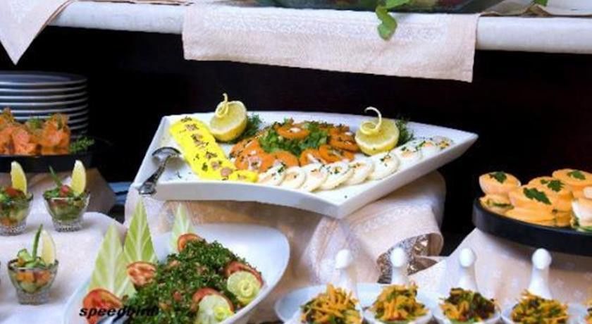 فندق مكارم أم القرى مكة المظهر الخارجي الصورة The photo shows a beautifully arranged platter of food. On a triangular white plate, there are neatly arranged slices of smoked salmon, garnished with lemon slices and some herbs. Surrounding the salmon are other items that appear to be slices of a l
