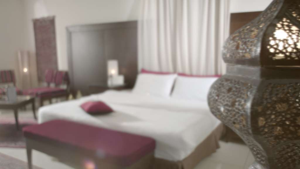 فندق مكارم أم القرى مكة الغرفة الصورة The image depicts a bedroom with a modern and elegant design. In the foreground, there is a large, neatly made bed with white linens and a purple decorative pillow. To the side, there is a long bench in a matching purple color. The background feature