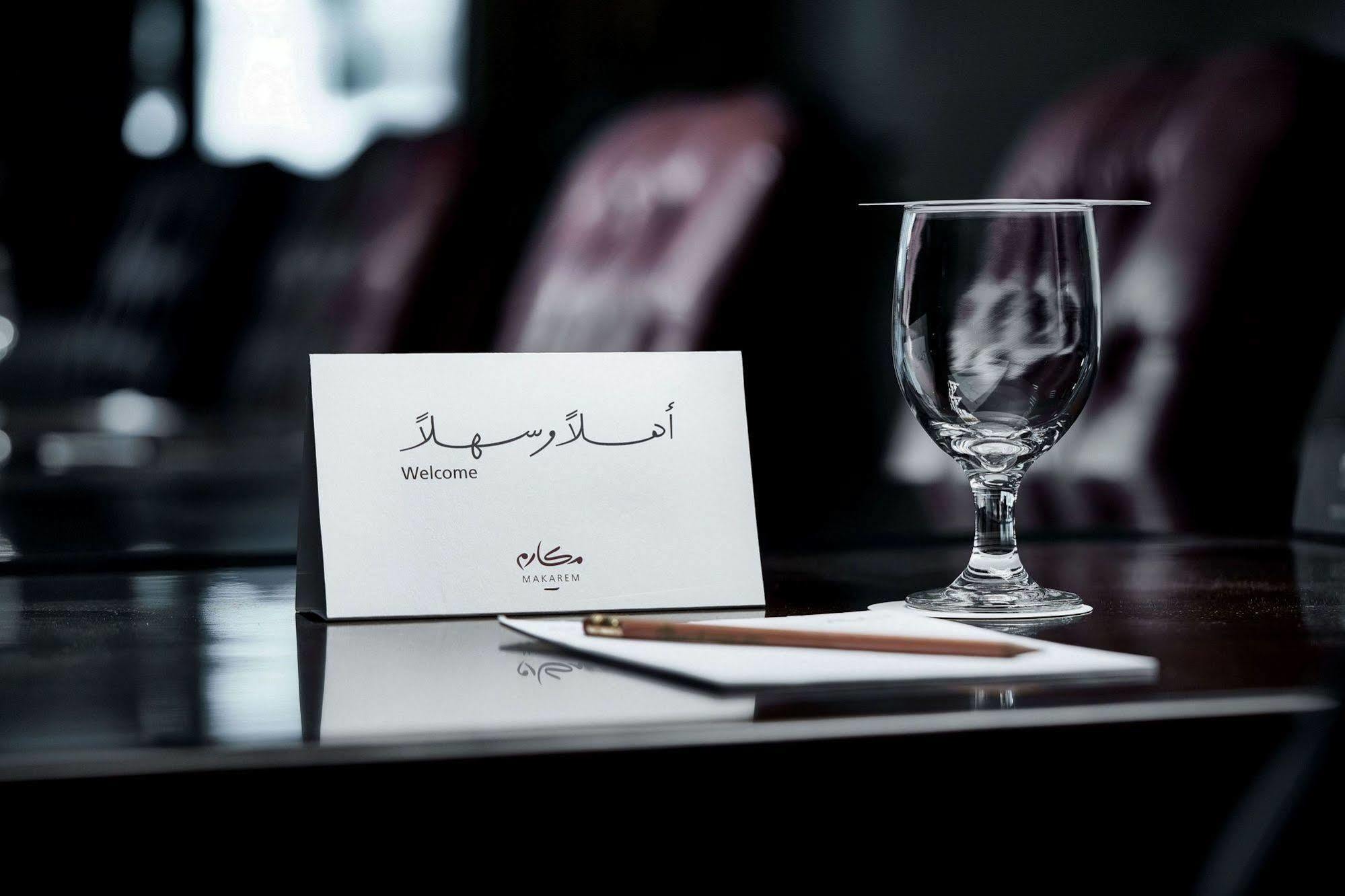 فندق مكارم أم القرى مكة المظهر الخارجي الصورة The photo depicts a refined setup on a polished table. There is a small welcome card, which includes the word "Welcome" written in English, alongside Arabic script. Also present is a clear glass, presumably for drinking, and a wooden pencil resting o