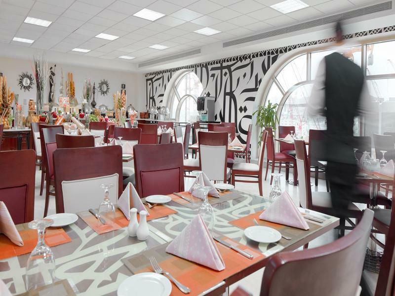 فندق مكارم أم القرى مكة المظهر الخارجي الصورة The photo shows an interior of a restaurant featuring a modern and elegant design. The dining area includes tables set with white plates, folded napkins, and glassware. The furniture consists of brown and white chairs arranged around the tables. A la